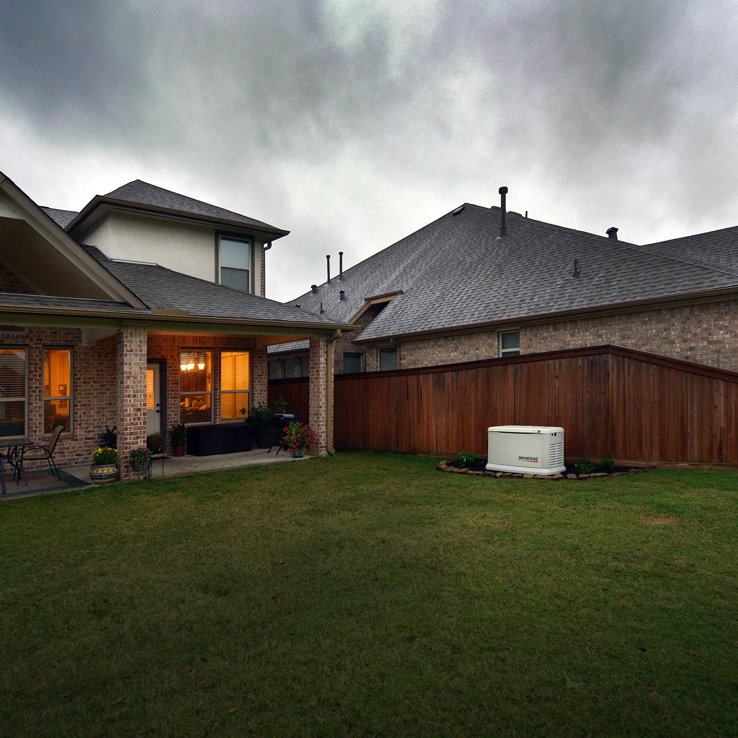 Generac standby generator installed in a residential backyard beside a fenced home.