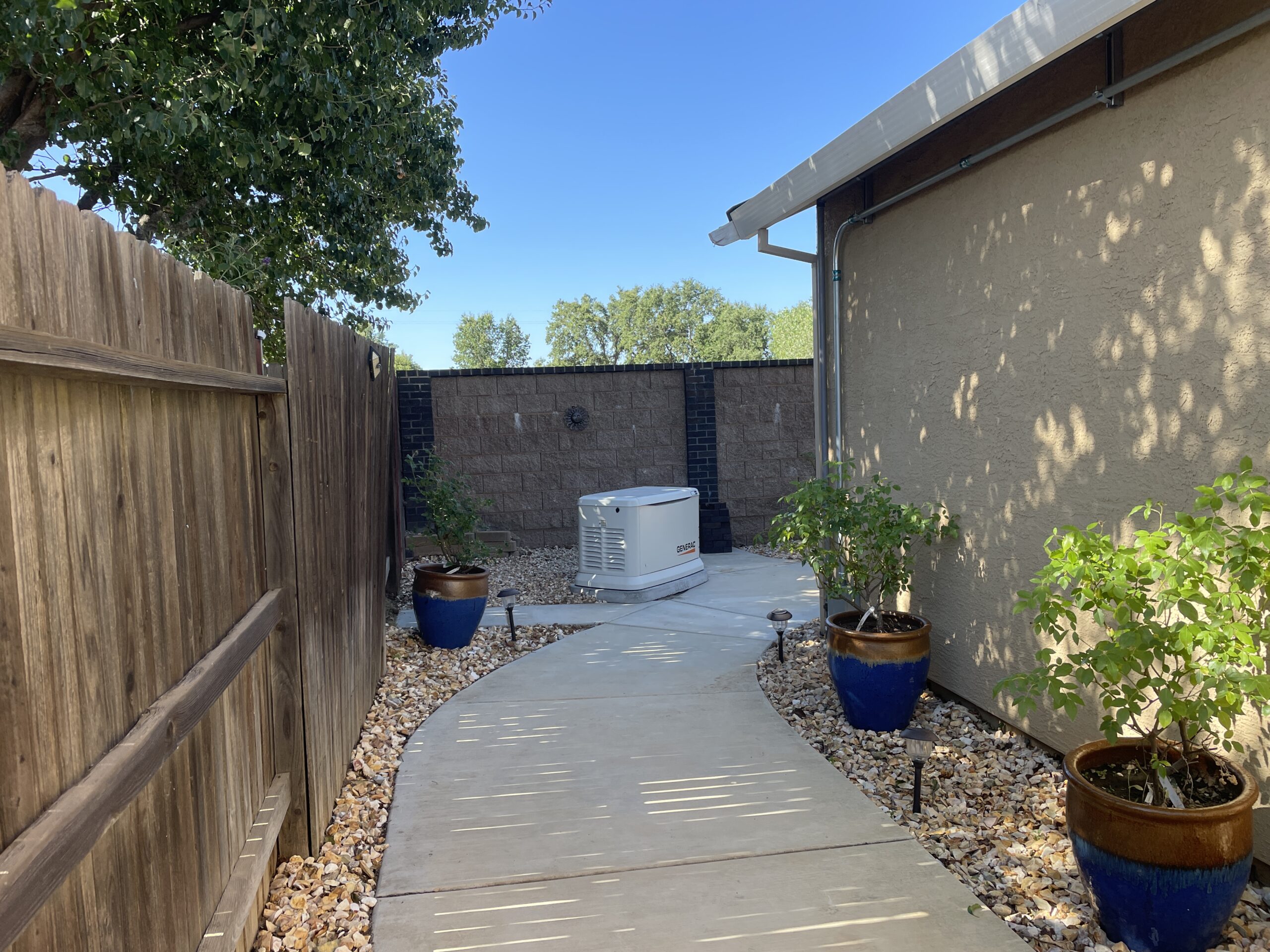 Generac standby generator installed on a concrete pad along a side yard walkway of a home.